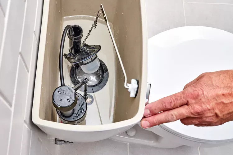 A person is pressing a button on a toilet tank. A person is pressing a button on a toilet tank.