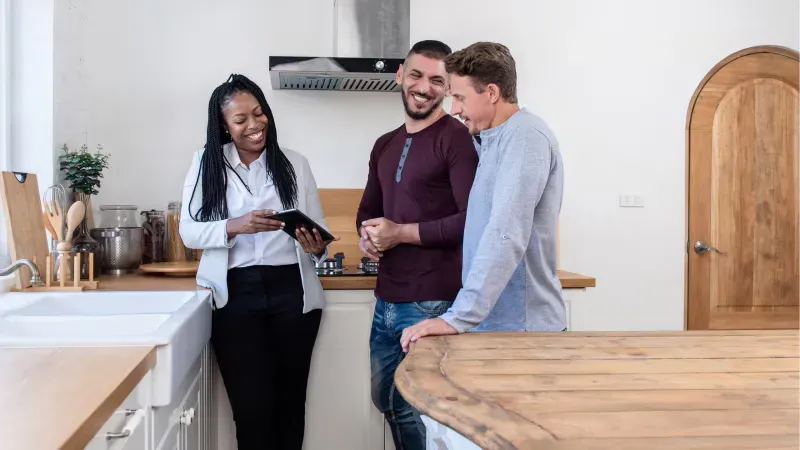 A woman is standing next to two men in a kitchen. A woman is standing next to two men in a kitchen.
