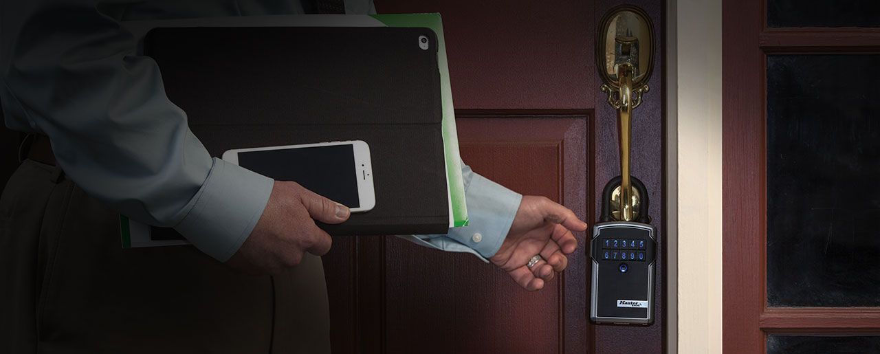 A man is holding a laptop and a cell phone while opening a door.