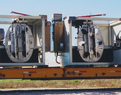 Two large industrial machine units mounted on a railcar under a clear sky.