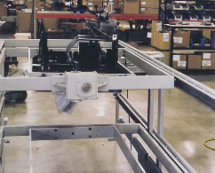 Industrial machine on a factory floor with metal rails and a central white carriage.