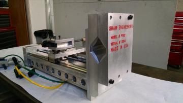 Silver machine on a table with a black component, yellow cable, and red warning text on the front panel