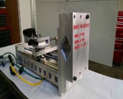 Metal mechanical assembly machine with silver frame, yellow hose, and red text on the side in a workshop