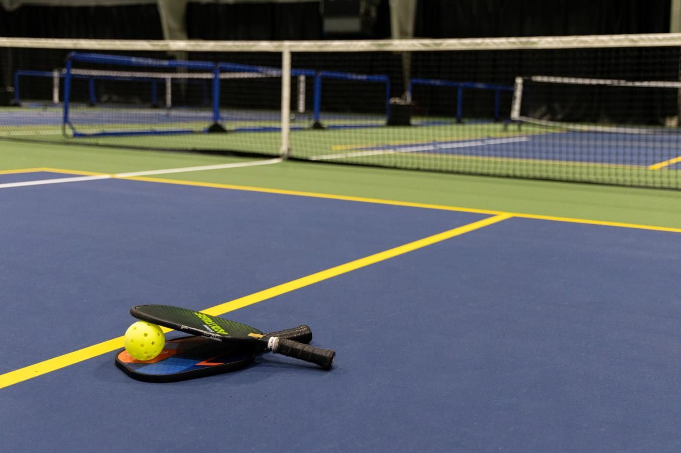 Pickleball paddles and ball on a blue court with a net in the background.