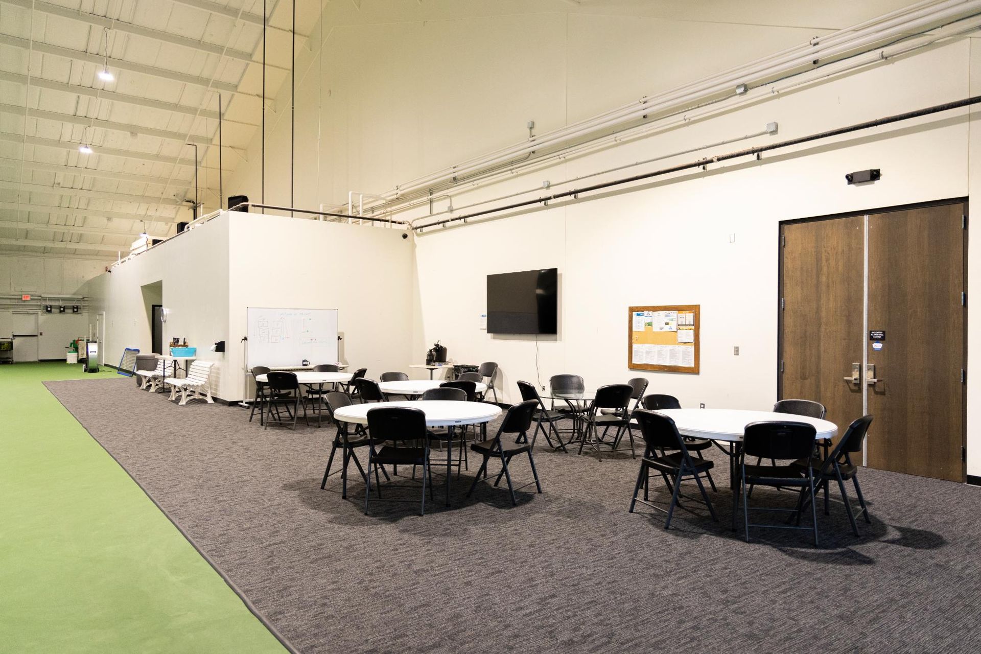 Indoor recreation area with tables and chairs, a TV, and a bulletin board.