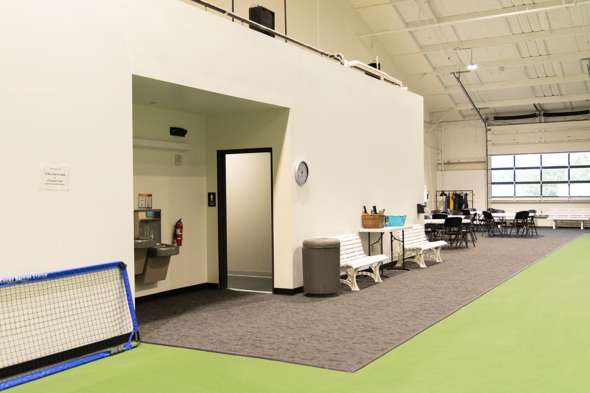 Indoor recreational area: white walls, gray carpet, green floor, water fountain, door, benches, and tables.