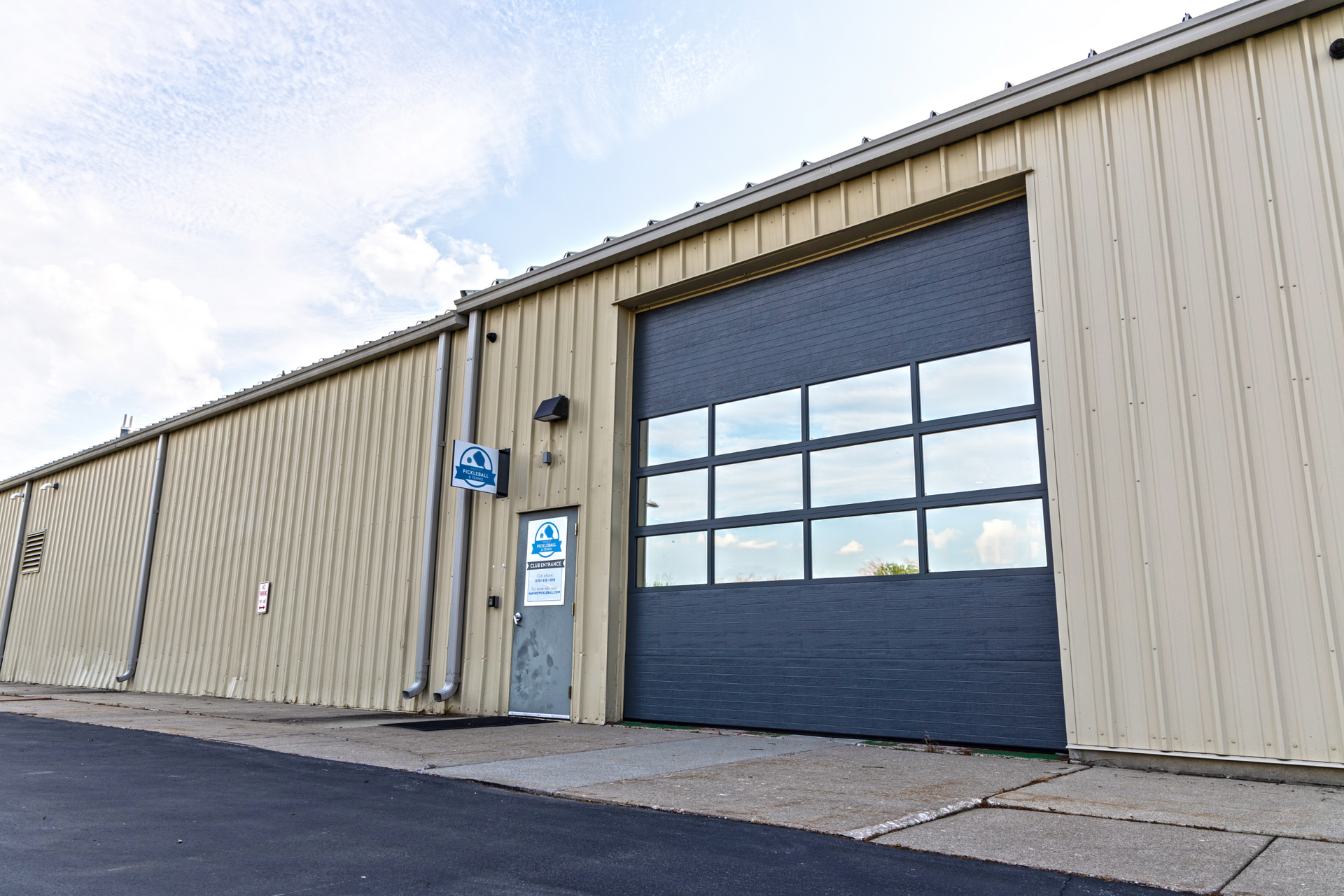 Warehouse exterior with a large gray door and smaller door, beige siding, and blue sky.