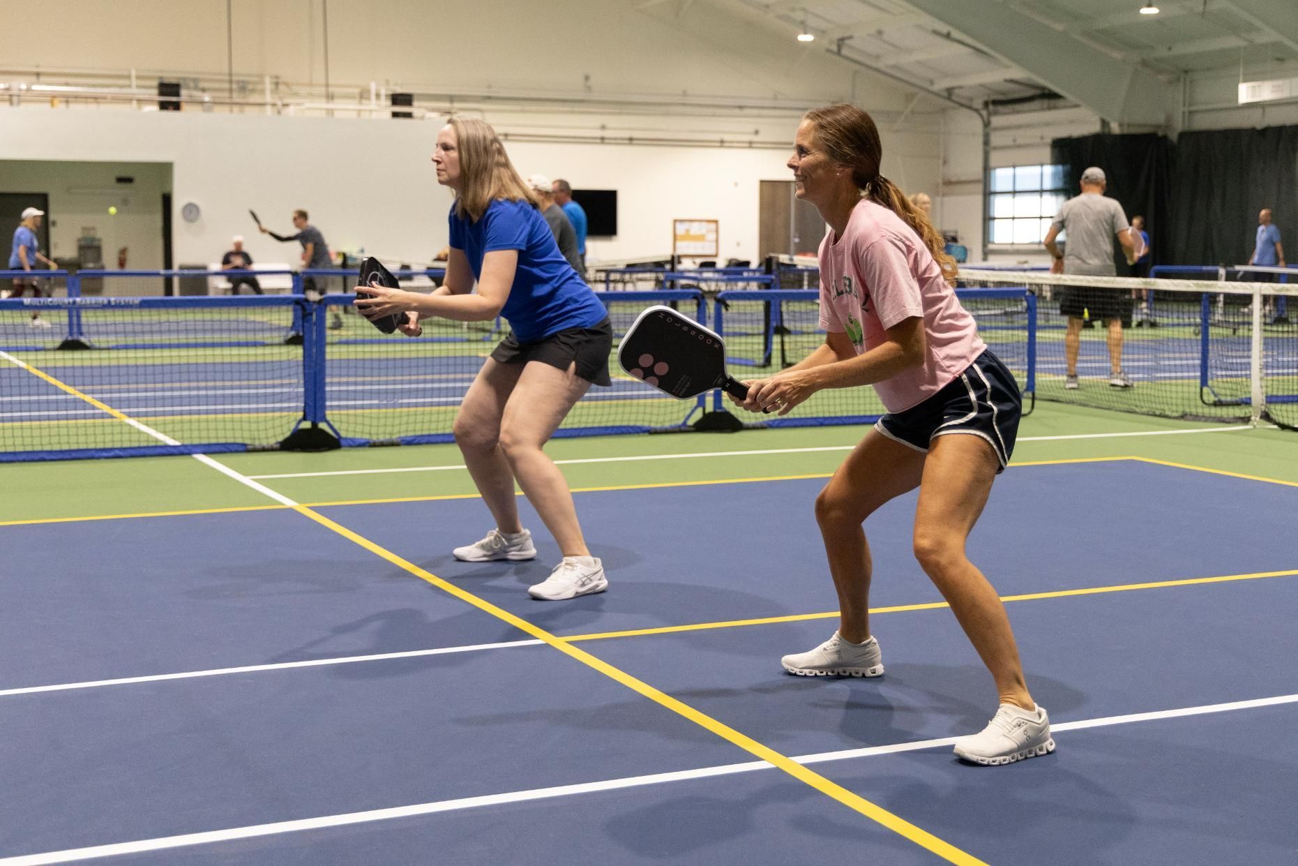 Two women playing pickleball indoors on blue court.