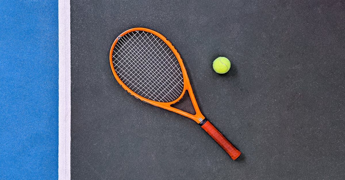 Tennis racket and ball on a dark court, near a blue sideline.