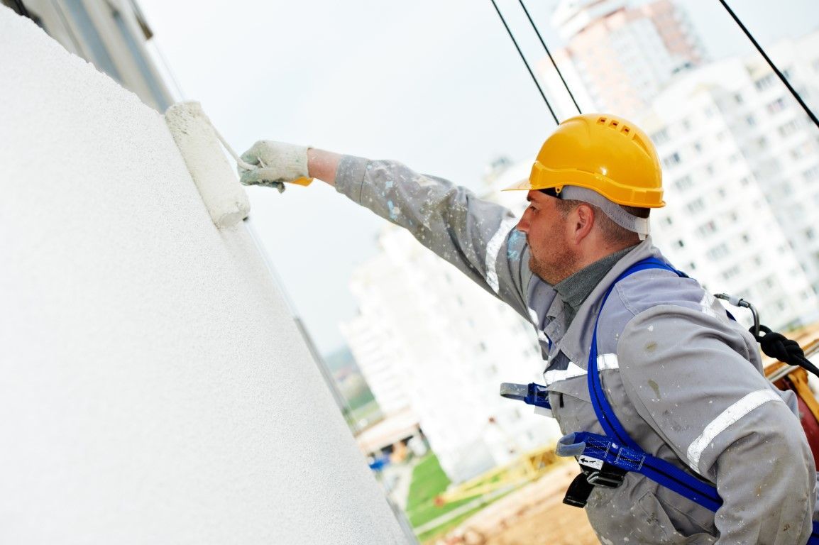 Construction worker in yellow hard hat painting a white wall on scaffolding
