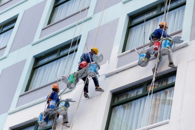 Three window cleaners suspended on ropes cleaning windows of a tall building