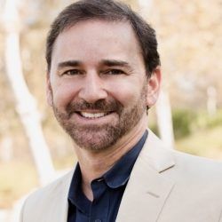 A man with a beard is wearing a tan suit and smiling for the camera.