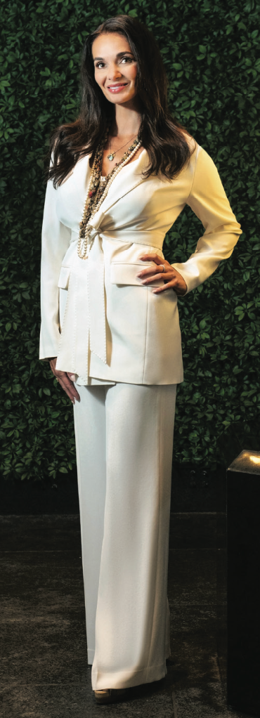 A woman in a white suit is standing in front of a green wall