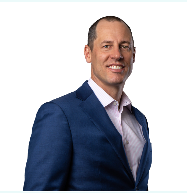 A man in a blue suit and pink shirt is smiling