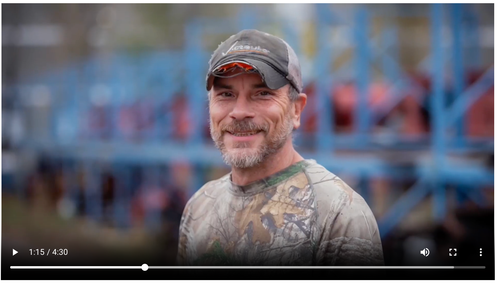 A man wearing a hat and a camo shirt is smiling for the camera.