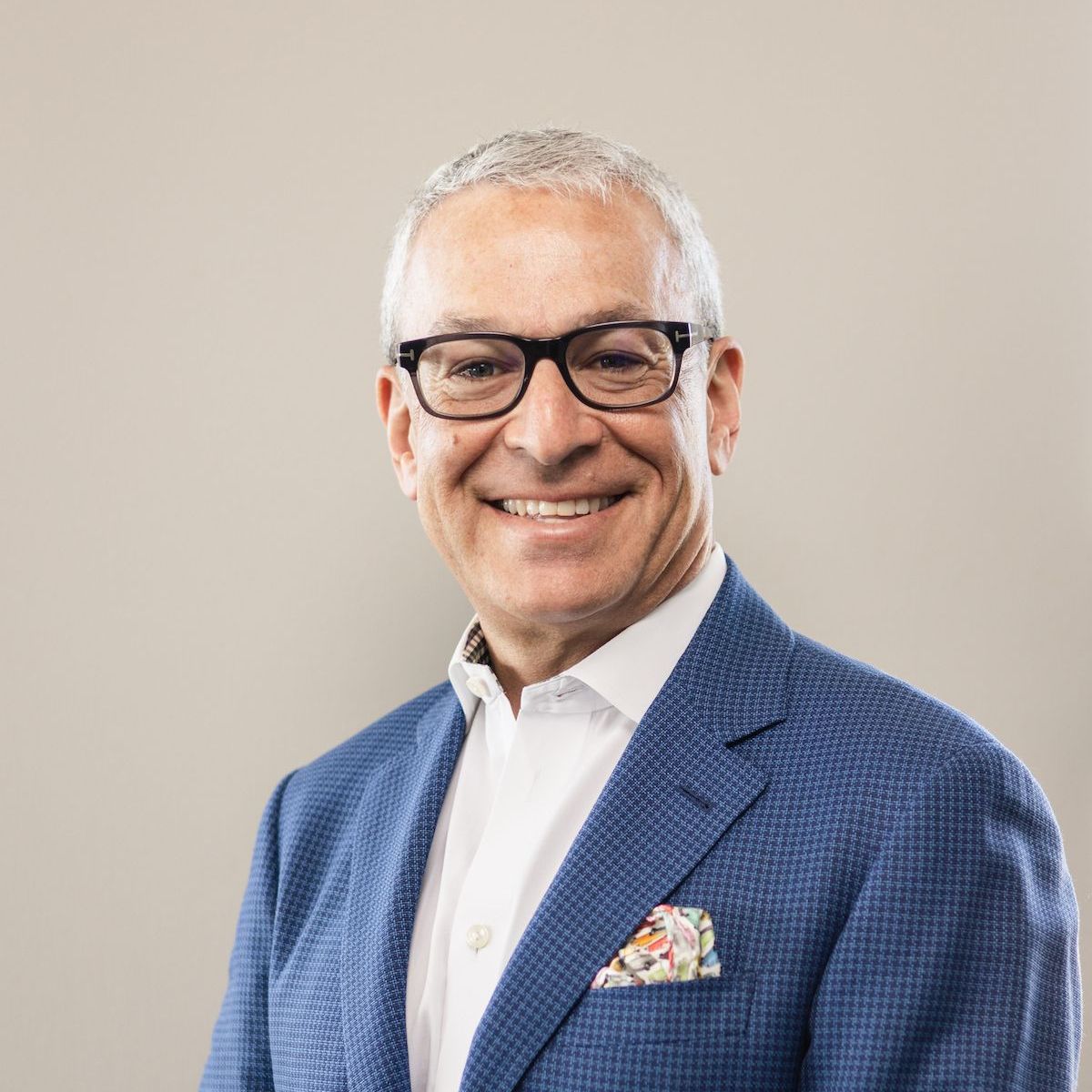 A man wearing glasses and a blue jacket is smiling for the camera.