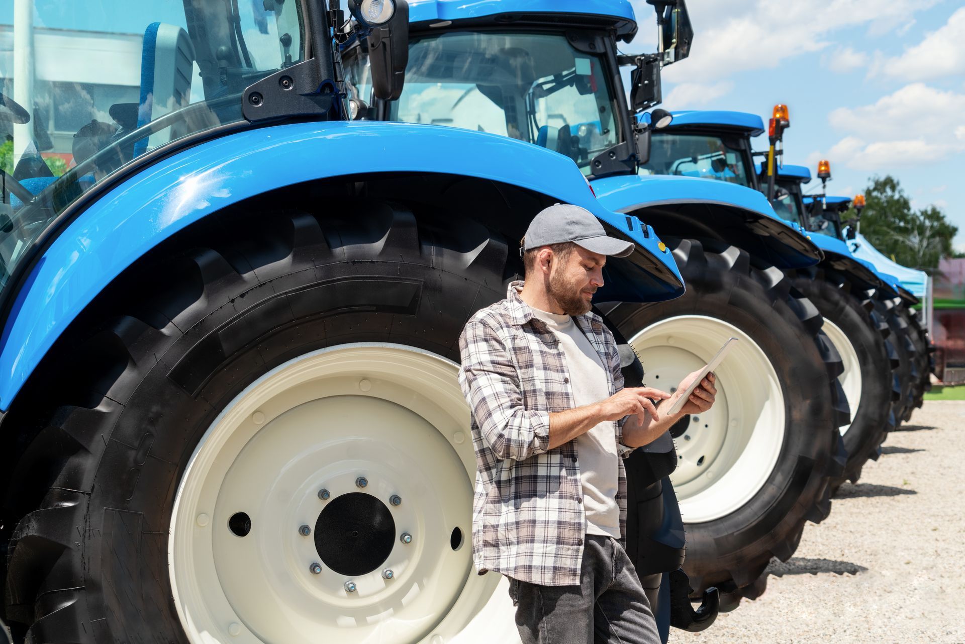 A man leaning against a blue tractor looking at a tablet