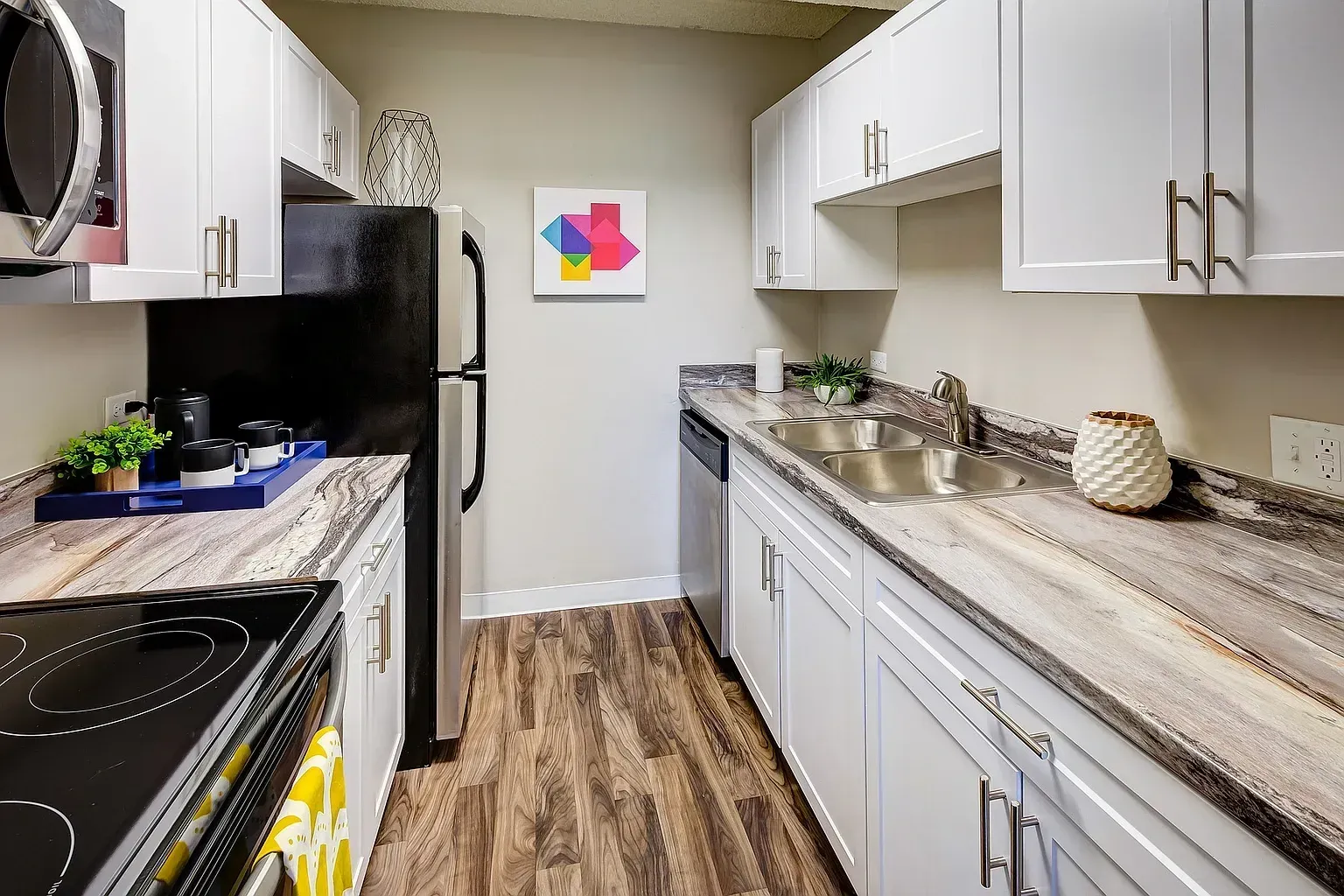 Modern kitchen with white cabinets, granite countertops, stainless steel appliances, and wood-look flooring.
