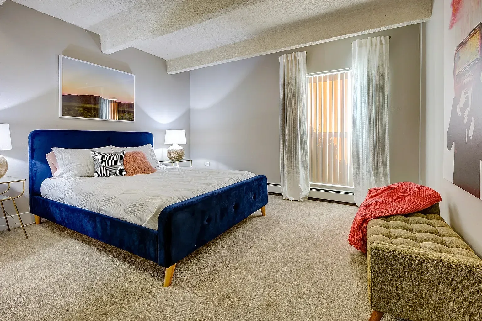 Modern bedroom with a navy blue velvet bed and plush white bedding, complemented by a stylish bench and artwork.