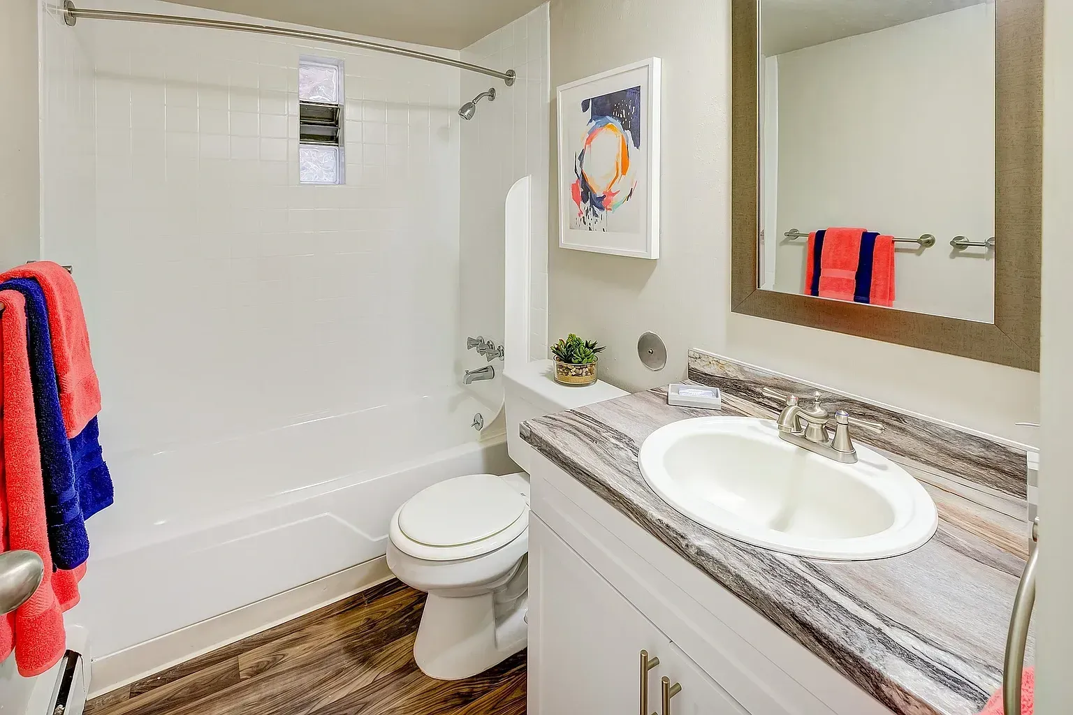 Modern bathroom with a white tub, toilet, and vanity with a marble countertop.