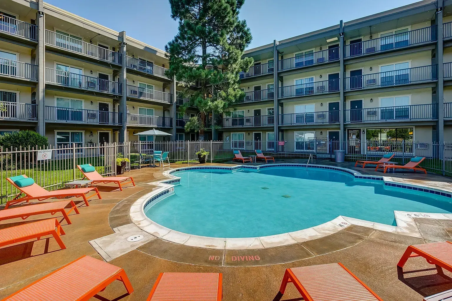 Resort-style swimming pool with lounge chairs and a courtyard building.