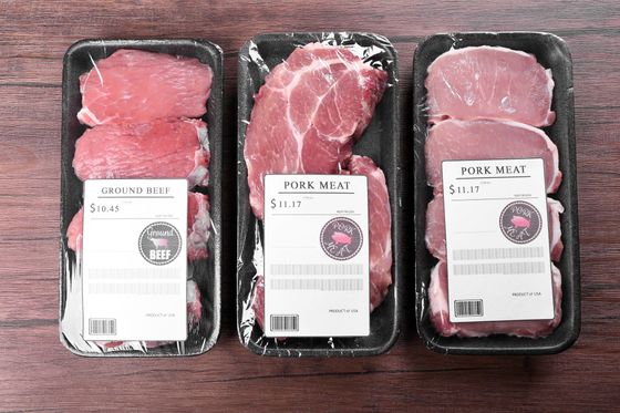 Three packaged raw beef steaks in black trays on a wooden table, each with a white label.