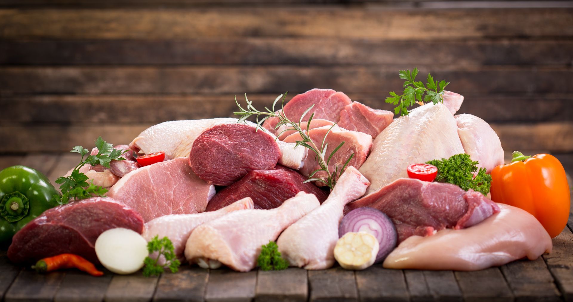 Assorted raw meats and vegetables arranged on a wooden table with herbs and spices. Assorted raw meats and vegetables arranged on a wooden table with herbs and spices.