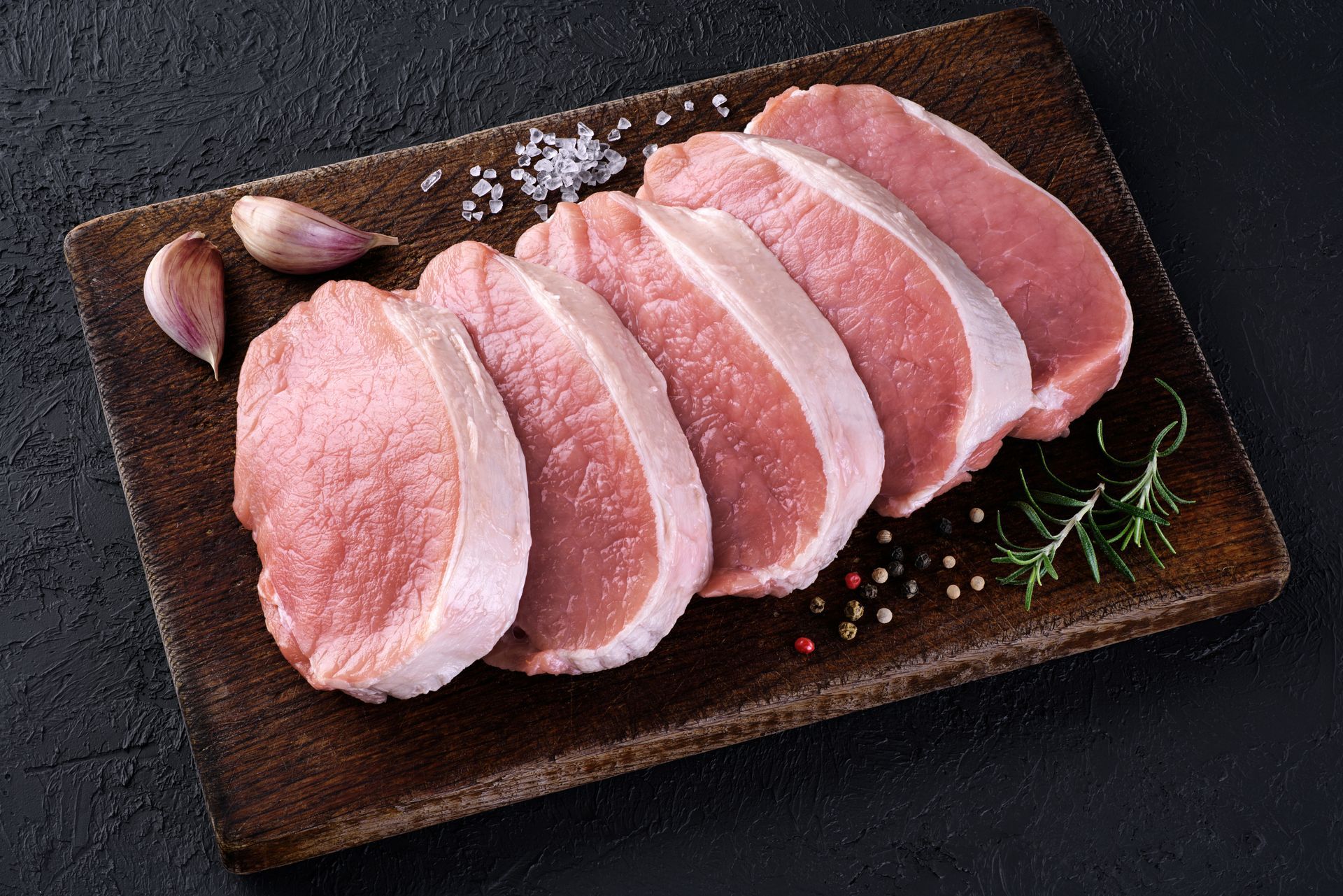 Raw pork chops arranged on a dark plate with garlic and herbs Raw pork chops arranged on a dark plate with garlic and herbs