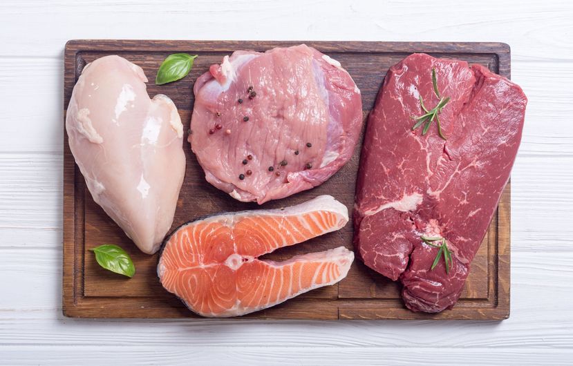 Raw meats and salmon fillet on a wooden cutting board with herb garnish