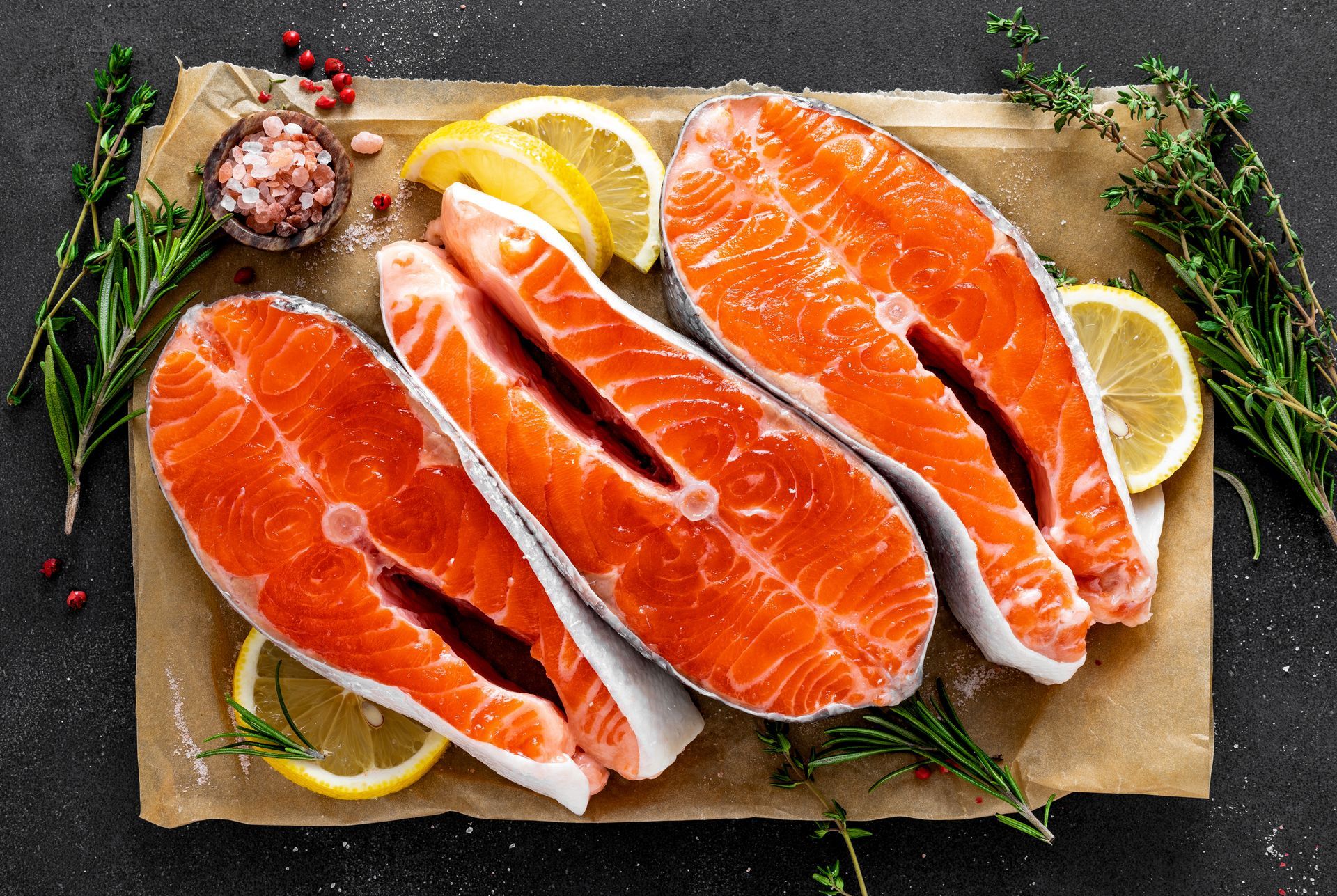 Raw salmon fillets with lemon wedges and herbs on parchment paper