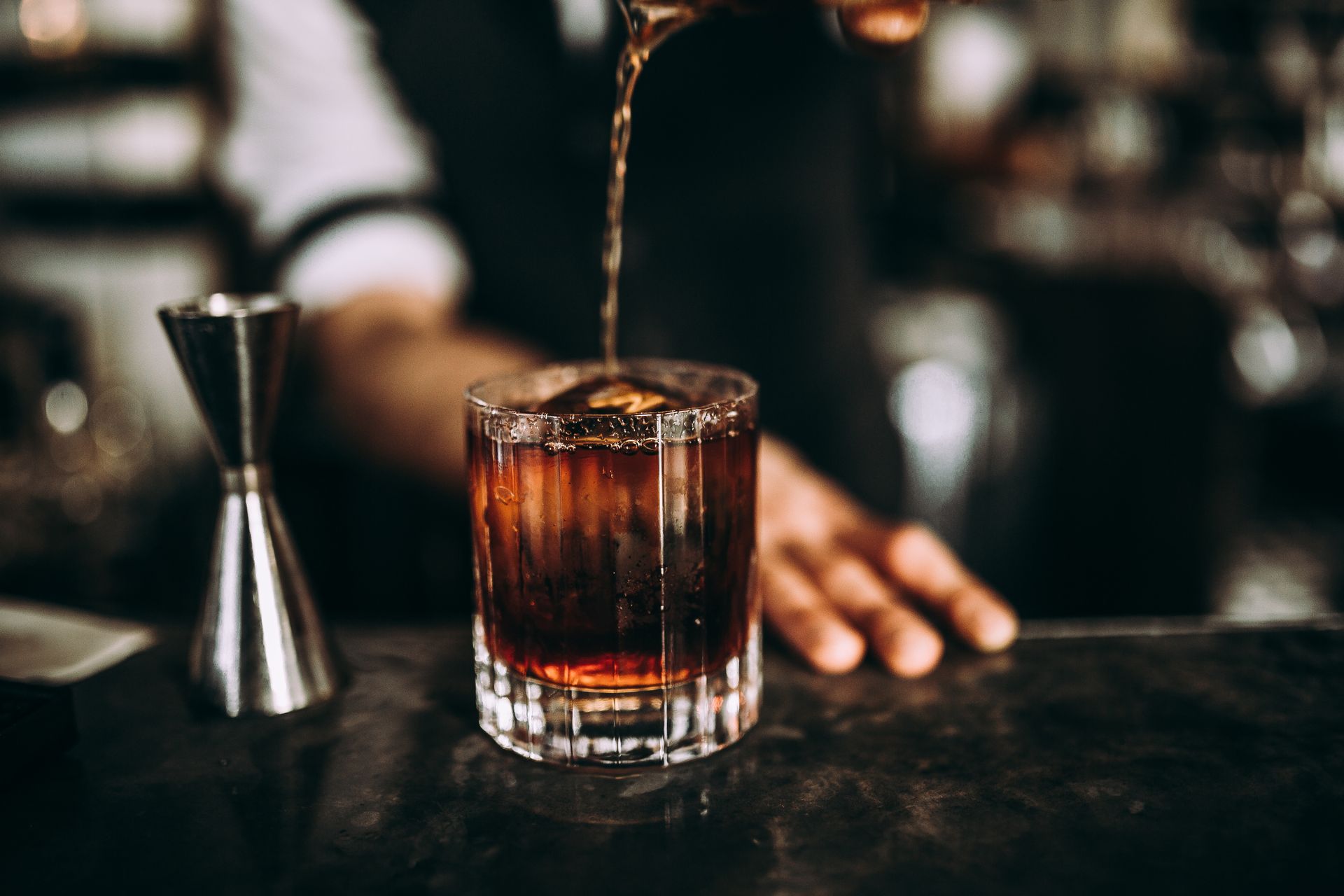 Whiskey being poured into a rocks glass on a bar, with a jigger beside it. Whiskey being poured into a rocks glass on a bar, with a jigger beside it.
