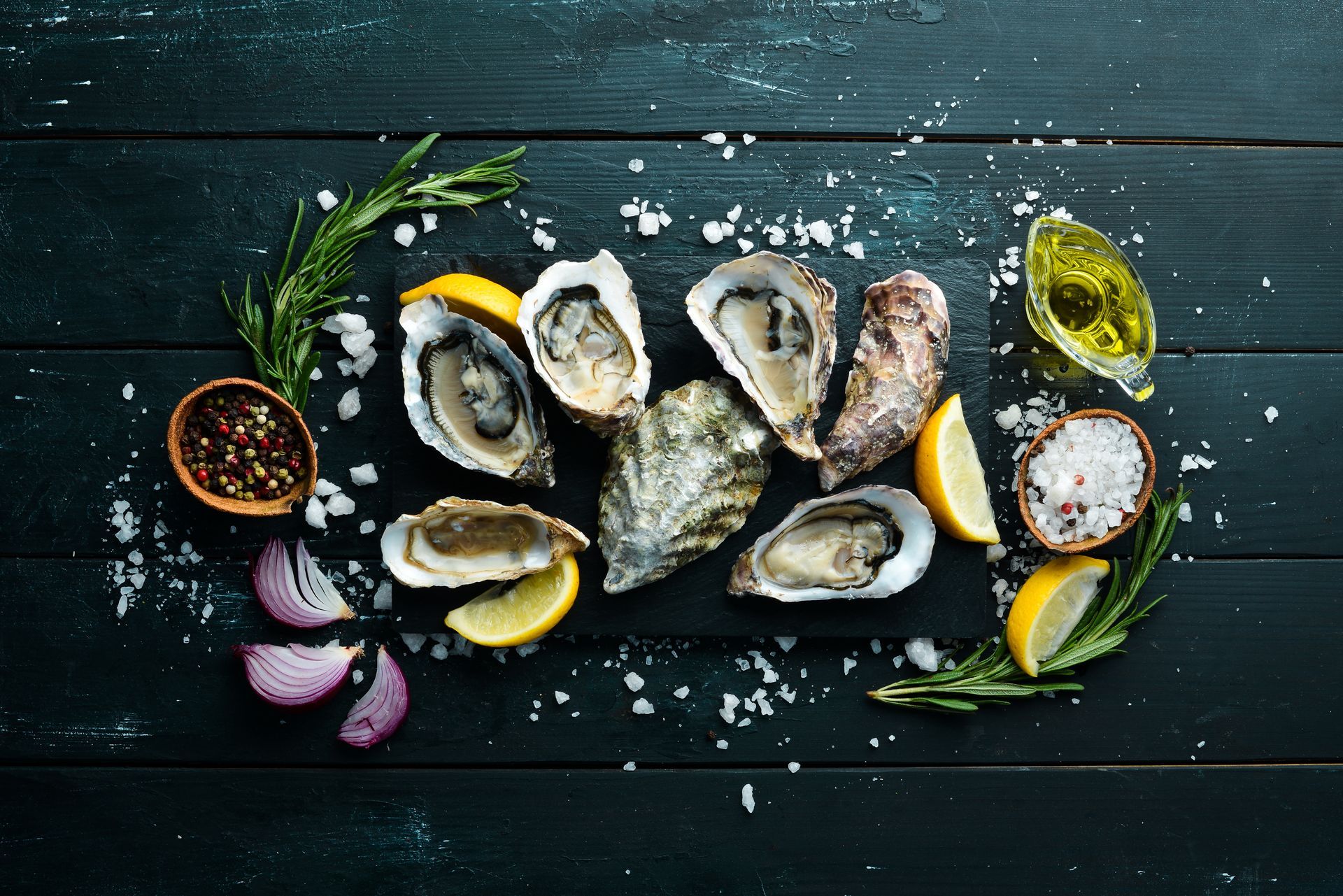 Fresh oysters on a dark wooden table with lemon wedges, herbs, salt, and dipping sauce
