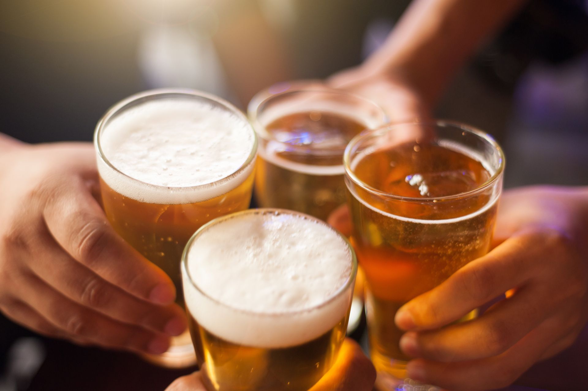 Hands clinking beer glasses at a bar, with foamy pints and amber drinks visible Hands clinking beer glasses at a bar, with foamy pints and amber drinks visible