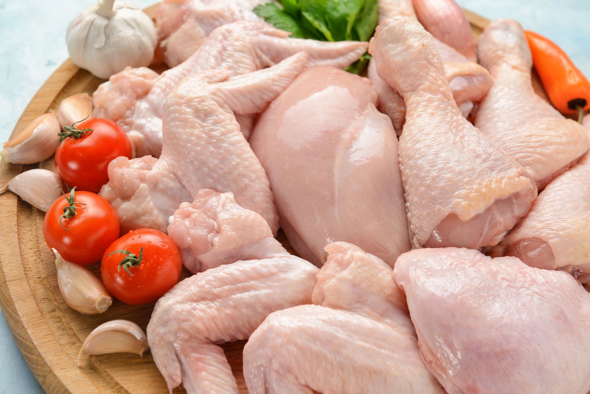 Raw chicken pieces with cherry tomatoes and garlic on a wooden cutting board Raw chicken pieces with cherry tomatoes and garlic on a wooden cutting board