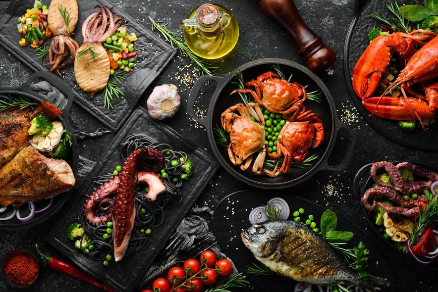 Seafood assortment on dark slate plates: shrimp, mussels, crab, octopus, lemon, and herbs