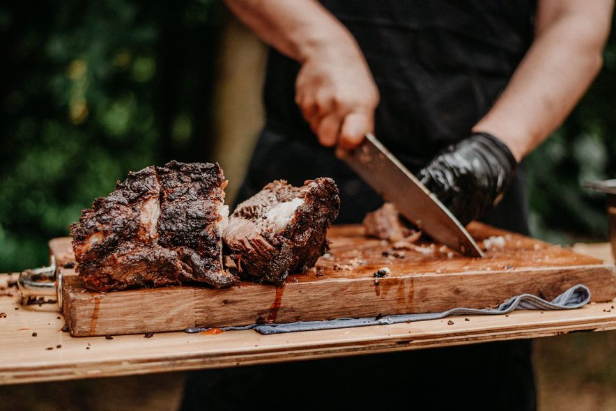 Person slicing grilled meat on a wooden board outdoors