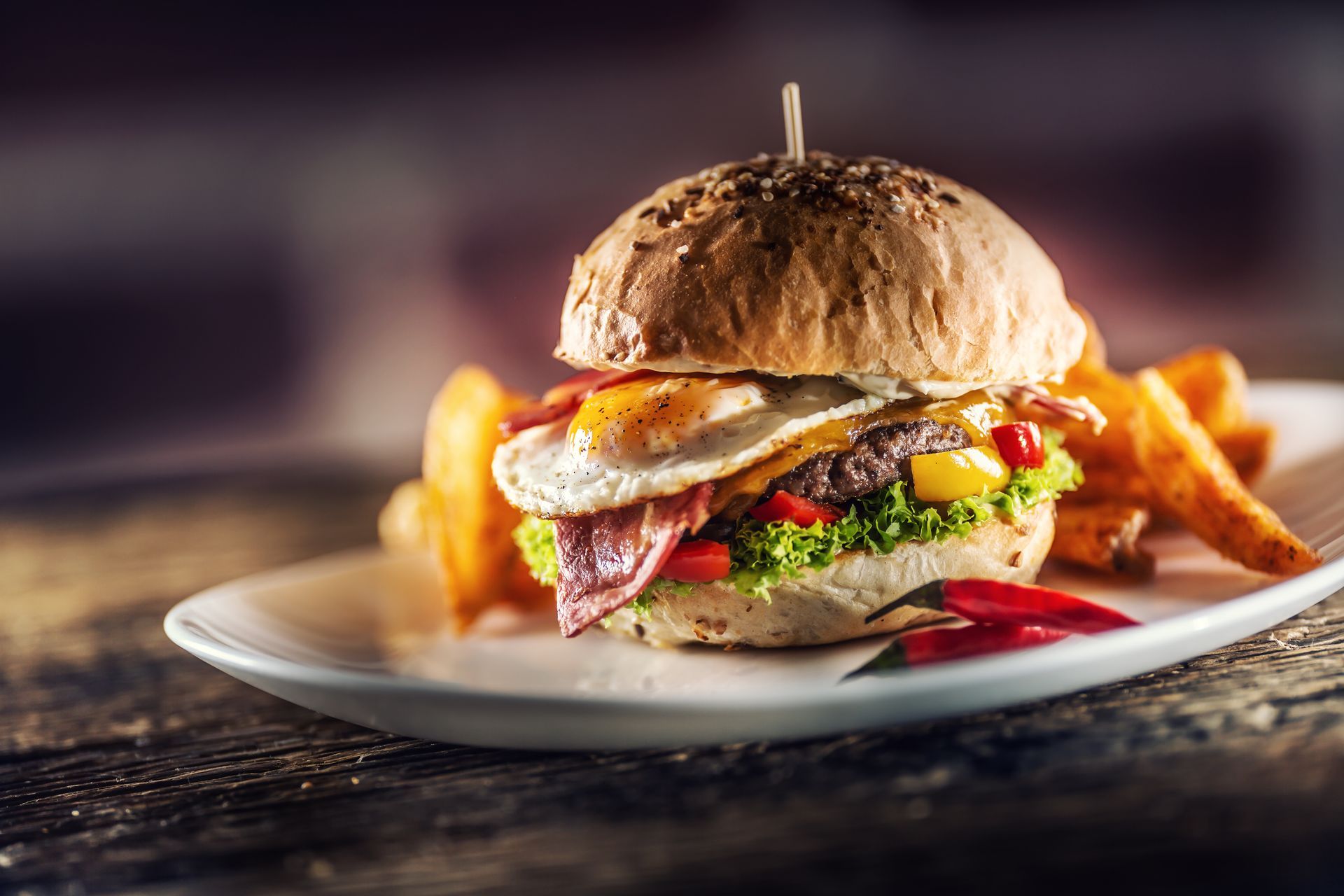 Burger with fries on a plate, topped with bacon and sauce, on a rustic table Burger with fries on a plate, topped with bacon and sauce, on a rustic table