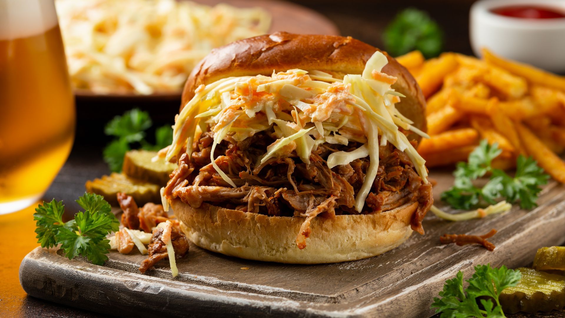 Pulled pork sandwich on a bun with melted cheese, fries, and a beer on a rustic wooden board Pulled pork sandwich on a bun with melted cheese, fries, and a beer on a rustic wooden board