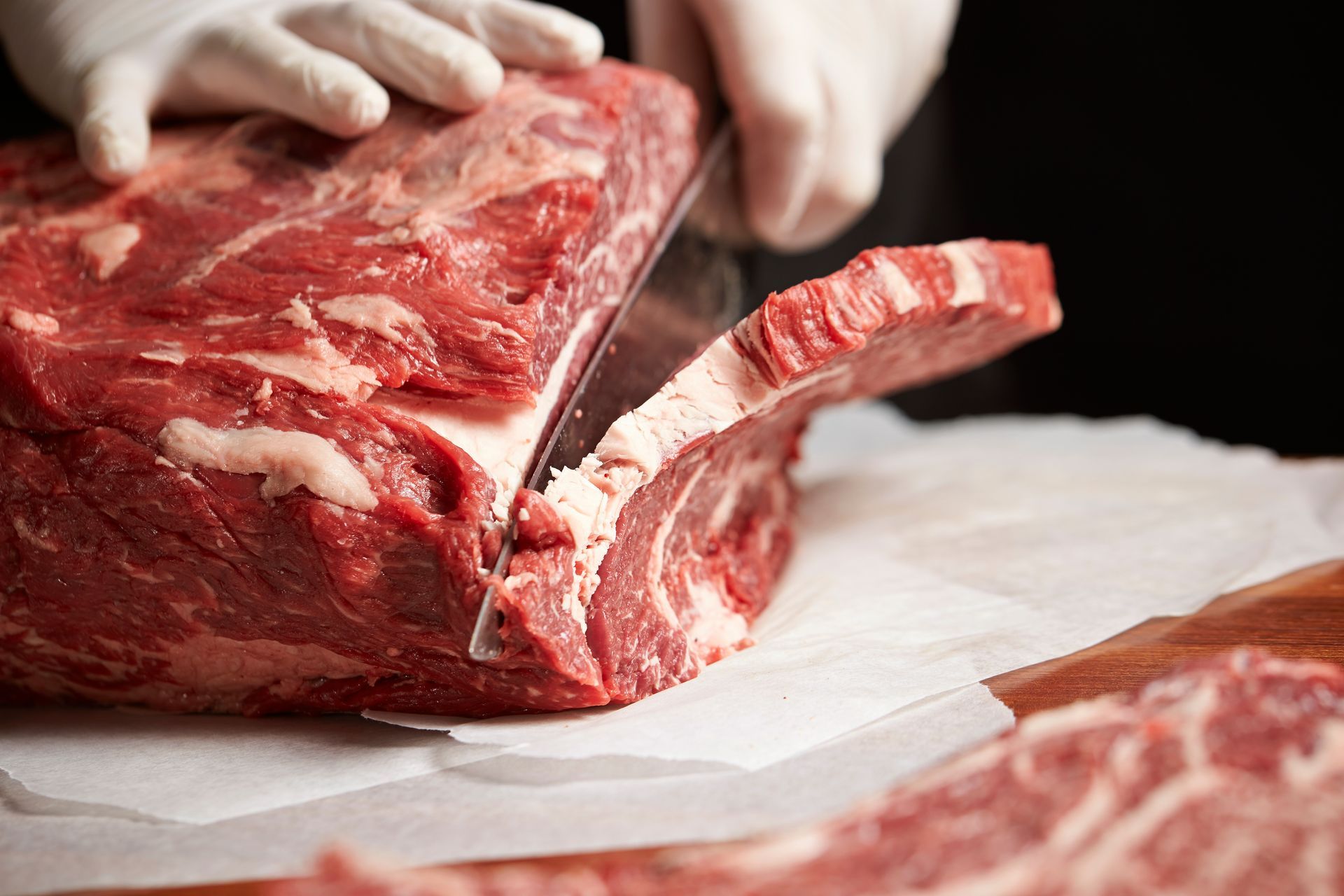 Hands slicing a raw red meat roast on a cutting board with a large knife Hands slicing a raw red meat roast on a cutting board with a large knife
