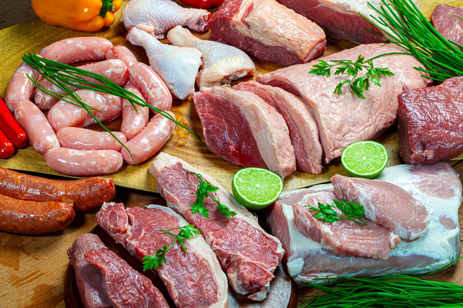 Assorted raw meats and sausages arranged on a wooden surface with herbs and lime slices Assorted raw meats and sausages arranged on a wooden surface with herbs and lime slices