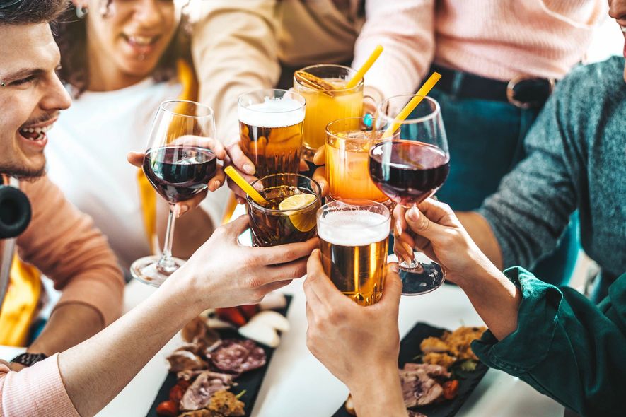 Friends clinking drinks around a table with beer, wine, and cocktails at a social gathering