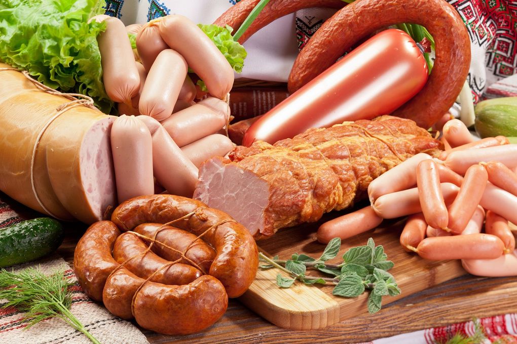 Assorted sausages, hot dogs, and cured meats arranged on a wooden board with lettuce and herbs