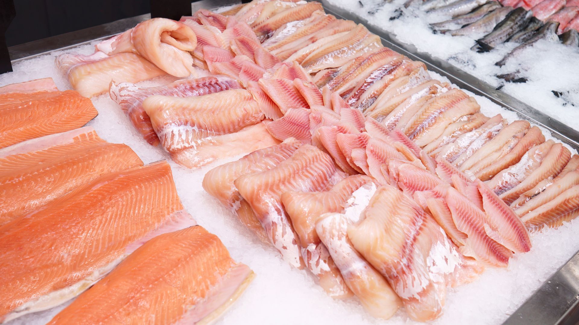 Assorted raw fish fillets and seafood displayed on ice at a market counter