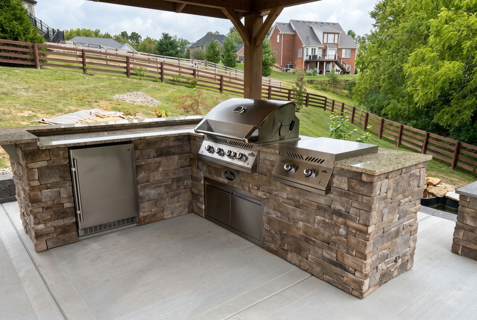 Stone patio fire pit with curved seating and lit lamps in a grassy backyard at dusk