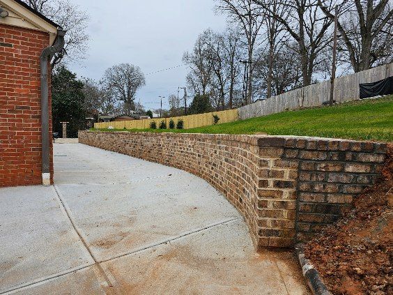 Curved concrete driveway beside a brick house and low brick retaining wall in a fenced yard
