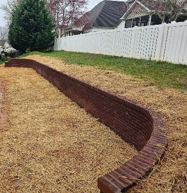 Curved red brick retaining wall along a sloped yard beside a white fence and house