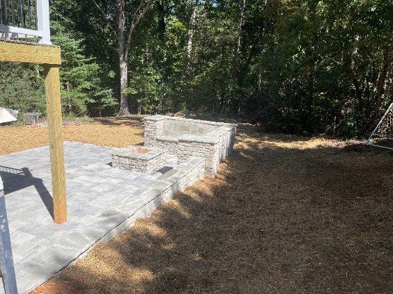 Wooden deck and stone patio beside a wooded backyard, with outdoor seating and steps.