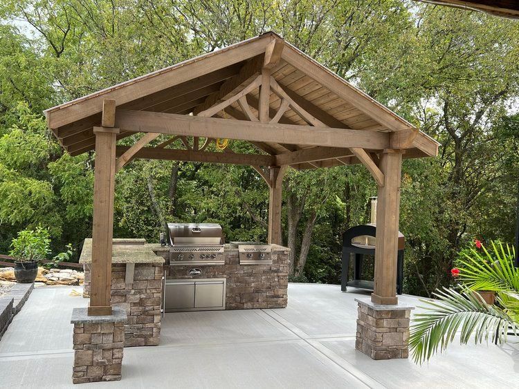 Wooden pavilion with stone grill and countertop in a landscaped outdoor patio area