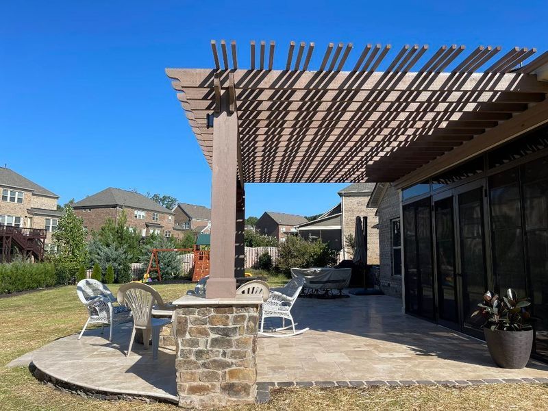 Patio with wooden pergola, stone column, white chairs, and potted plants beside a modern house