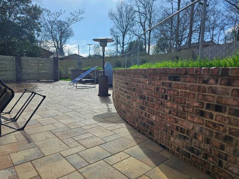 Sunny outdoor patio with brick wall, tiled paving, benches, and a playground slide in the background
